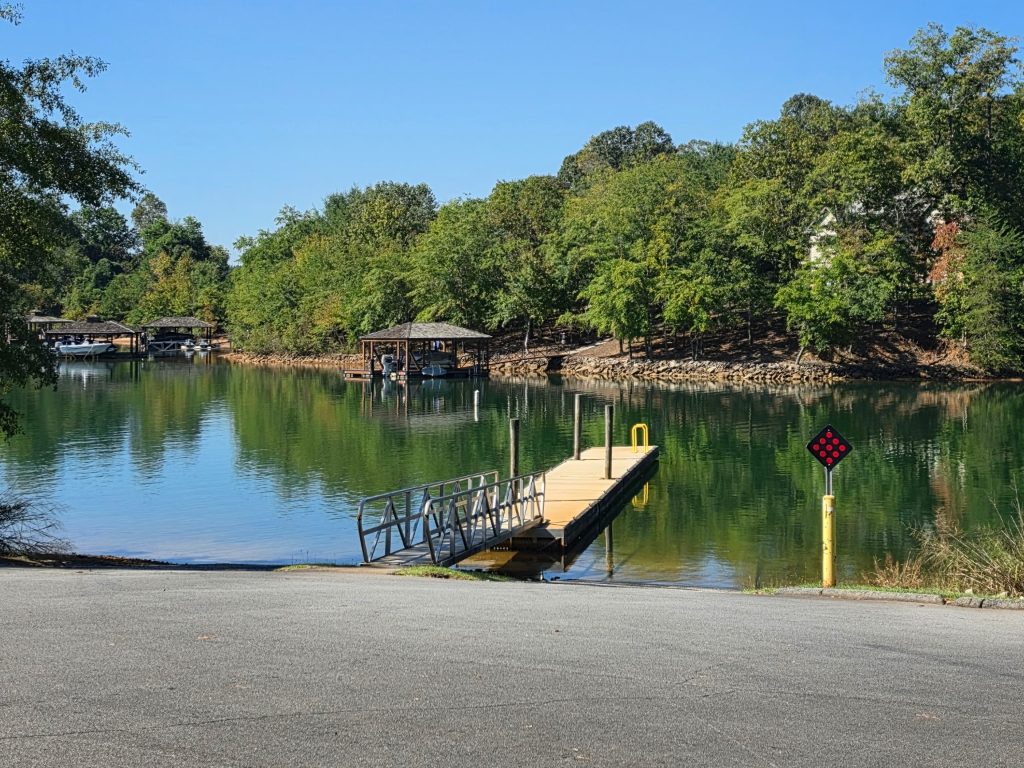 The Crowe Creek boat ramp running down to a floating dock on calm Lake Keowee, with covered boat docks along the far shore.